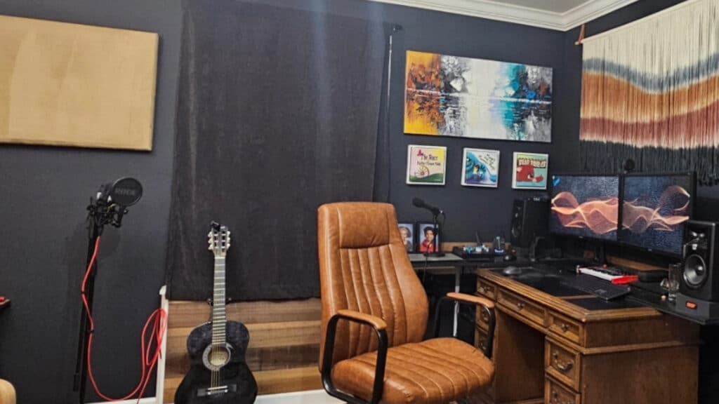 A picture of the desk of R.E. Lockett showing a guitar, leather chair, wooden desk, and computer with peripherals including speakers, microphone, mini keyboard and drawing tablet.